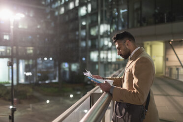 Geschäftsmann bei der Durchsicht von Papieren auf einer Fußgängerbrücke in der Nacht - CAIF21976