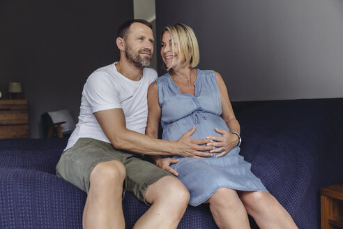 Reifer Mann und seine schwangere reife Frau sitzen auf dem Bett und berühren ihren Bauch - MFF04623