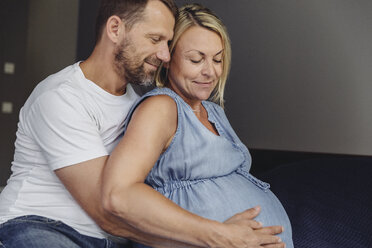Reifer Mann und seine schwangere reife Frau sitzen auf dem Bett und berühren ihren Bauch - MFF04625