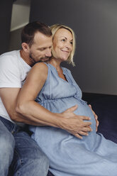 Reifer Mann und seine schwangere reife Frau sitzen auf dem Bett und berühren ihren Bauch - MFF04626