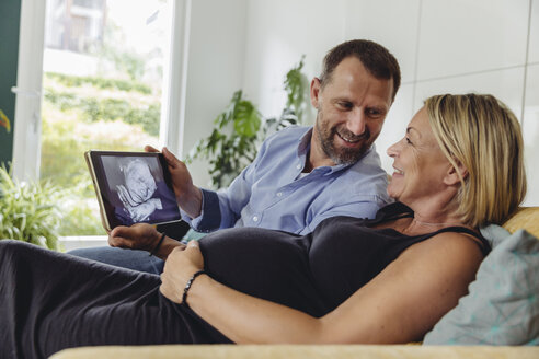 Älteres schwangeres Paar betrachtet ein 3D-Bild ihres ungeborenen Kindes auf einem Tablet-Computer - MFF04631