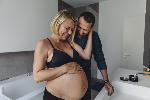 Glückliches reifes schwangeres Paar beobachtet den Bauch der werdenden Mutter im Badezimmer - MFF04638