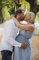 Mature pregnant couple kissing in park - MFF04642