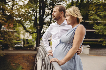 Mature pregnant couple standing at bridge in park - MFF04645