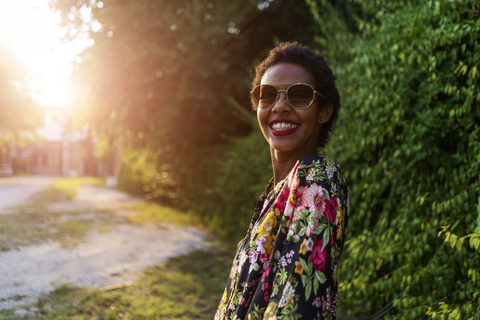 Porträt einer glücklichen jungen Frau mit Sonnenbrille im Freien bei Sonnenuntergang, lizenzfreies Stockfoto