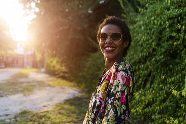 Porträt einer glücklichen jungen Frau mit Sonnenbrille im Freien bei Sonnenuntergang - GIOF04311
