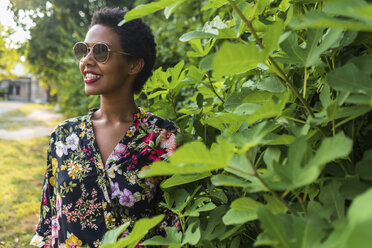 Lächelnde junge Frau mit Sonnenbrille und bunter Bluse in einem Park - GIOF04313