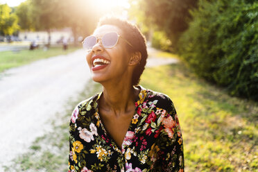 Lachende junge Frau mit Sonnenbrille im Freien bei Sonnenuntergang - GIOF04316