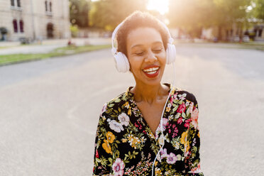 Happy fashionable young woman with headphones outdoors at sunset - GIOF04320