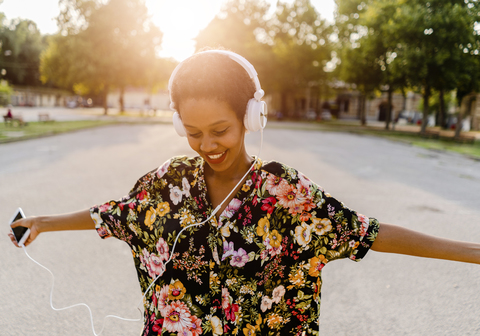 Happy fashionable young woman with headphones dancing outdoors at sunset stock photo