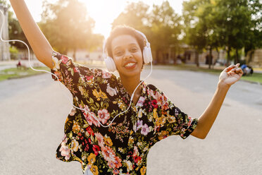 Happy fashionable young woman with headphones dancing outdoors at sunset - GIOF04324
