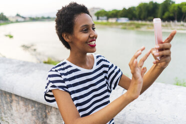 Smiling young woman using cell phone at the riverside - GIOF04336