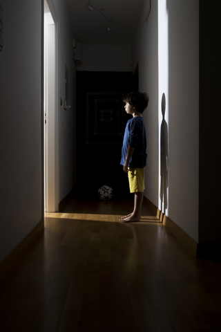 Einsamer kleiner Junge steht zu Hause im Flur und schaut auf die offene Tür, lizenzfreies Stockfoto