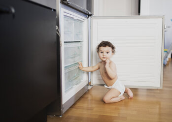 Porträt eines kleinen Jungen mit Windel, der vor dem Kühlschrank in der Küche hockt - AZOF00002