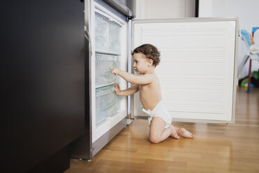 Ein kleiner Junge in einer Windel erkundet den Kühlschrank in der Küche - AZOF00003