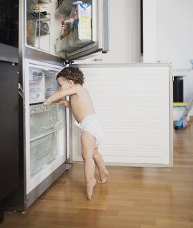 Baby boy wearing diaper exploring refrigerator in the kitchen - AZOF00004