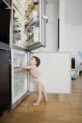 Ein kleiner Junge in einer Windel erkundet den Kühlschrank in der Küche - AZOF00005