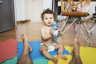 Porträt eines kleinen Jungen mit Windel, der zusammen mit seinem Vater auf dem Boden sitzt und Wasser trinkt - AZOF00009