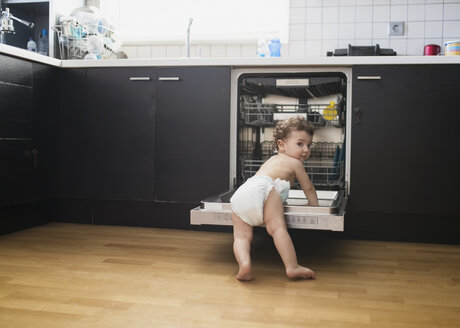 Porträt eines kleinen Jungen mit Windel, der die Spülmaschine in der Küche untersucht - AZOF00011