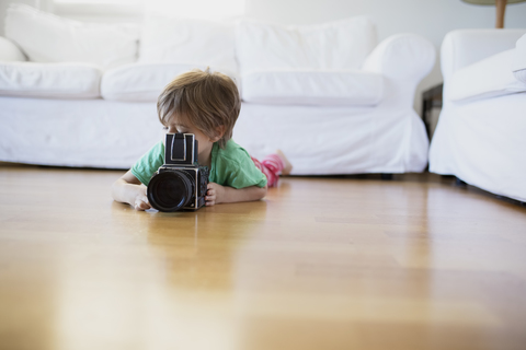 Kleiner Junge, der zu Hause auf dem Boden liegt und eine altmodische Filmkamera benutzt, lizenzfreies Stockfoto