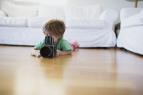 Kleiner Junge, der zu Hause auf dem Boden liegt und eine altmodische Filmkamera benutzt - AZOF00015