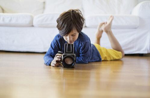Junge, der zu Hause auf dem Boden liegt und eine altmodische Filmkamera benutzt - AZOF00018