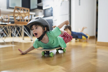 Kleinkind Junge zu Hause liegend auf Skateboard mit Helm Spaß haben - AZOF00023
