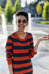 Porträt einer lachenden jungen Frau mit Sonnenbrille und gestreiftem Pullover - GIOF04338