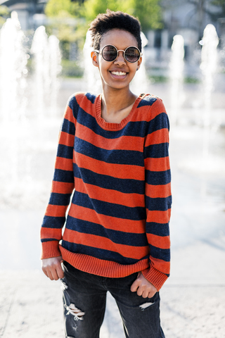 Porträt einer lächelnden jungen Frau mit Sonnenbrille und gestreiftem Pullover, lizenzfreies Stockfoto