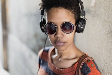 Porträt einer jungen Frau mit Sonnenbrille, die mit Kopfhörern Musik hört - GIOF04345