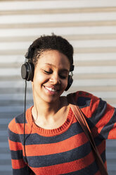 Porträt einer lächelnden jungen Frau, die mit Kopfhörern Musik hört - GIOF04350