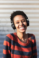Porträt einer lachenden jungen Frau, die mit Kopfhörern Musik hört - GIOF04351