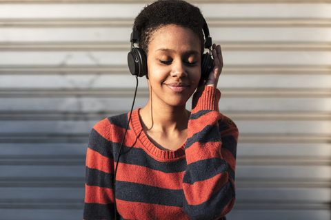 Porträt einer lächelnden jungen Frau, die mit Kopfhörern Musik hört, lizenzfreies Stockfoto