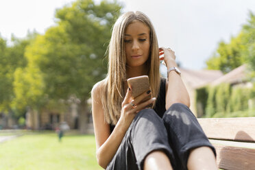 Relaxed teenage girl sitting on a bench using cell phone - GIOF04356