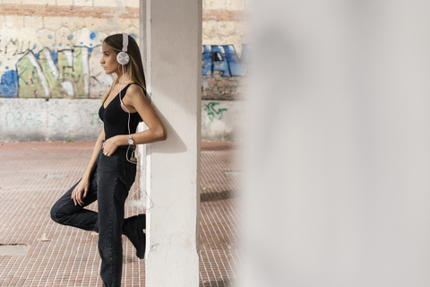 Teenager-Mädchen lehnt an einer Säule und trägt Kopfhörer, lizenzfreies Stockfoto