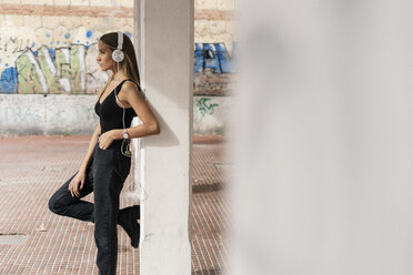 Teenage girl leaning at a column wearing headphones - GIOF04366