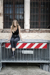 Portrait of smiling teenage girl sitting on barriers in the city - GIOF04372