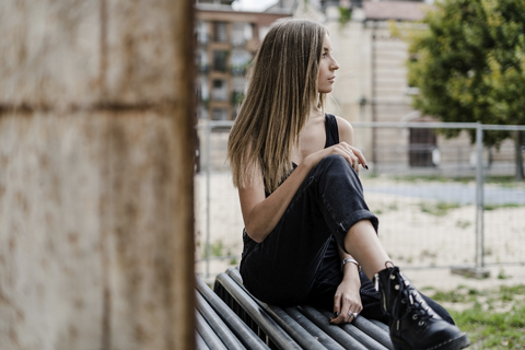 Nachdenkliches Teenager-Mädchen sitzt im Freien und schaut sich um, lizenzfreies Stockfoto