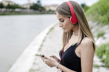 Teenage girl at the riverside wearing headphones using cell phone - GIOF04380