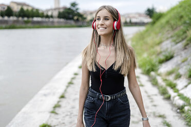 Smiling teenage girl at the riverside wearing headphones - GIOF04382