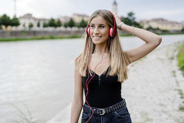 Smiling teenage girl at the riverside wearing headphones - GIOF04383