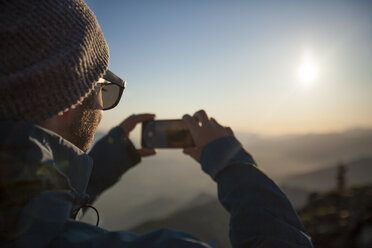 A man uses his phone to snap a photo of the view from the summit of Sauk Mountain. - AURF04071