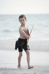 A young boy in a wetsuit holds his skim board while walking down the beach. - AURF04139