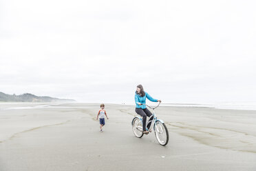 Eine Frau fährt mit dem Fahrrad neben einem kleinen Jungen am Strand. - AURF04146