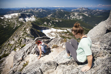 A young couple scramble down granite rock on the summit ridge of Needle Peak. - AURF04198