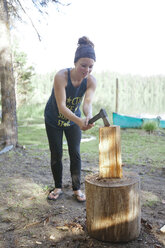 A young woman chops firewood with a small axe while camping at Unna Lake in Bowron Lake Provincial Park - AURF04204