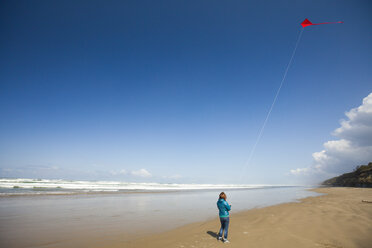 Eine junge Frau lässt einen roten Drachen in den Himmel steigen, während sie einen Strand an der Küste von Oregon besucht - AURF04210