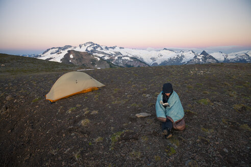 Eine junge Frau liest ein Buch beim Zelten auf der Panorama Ridge im Garibaldi Provincial Park, British Columbia, Kanada. - AURF04216