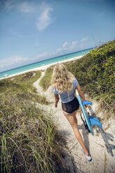 Eine junge Frau geht mit ihrem Surfbrett zum Strand. - AURF04234
