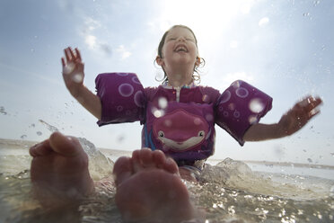 Ein junges Mädchen mit Schwimmflügeln planscht im Wasser am Strand. - AURF04259